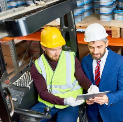 High angle portrait of mature businessman talking to warehouse worker sitting in forklift car, copy space