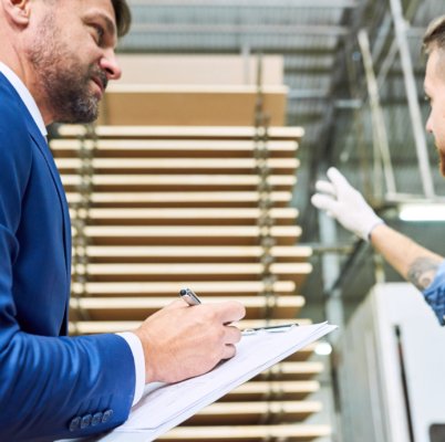 Side view portrait of handsome mature businessman touring modern factory inspecting quality of production, assisted with young workman