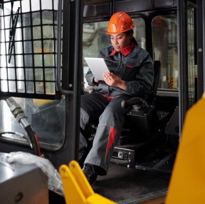 Young busy worker of factory with tablet scrolling through online technical data while sitting in construction machine